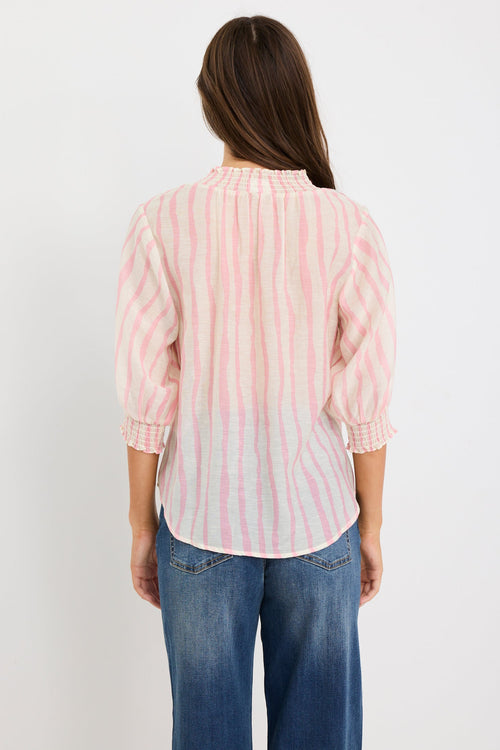 Woman wearing a blush and ivory stripe short sleeve top with a high neck and relaxed fit, styled with blue jeans.
