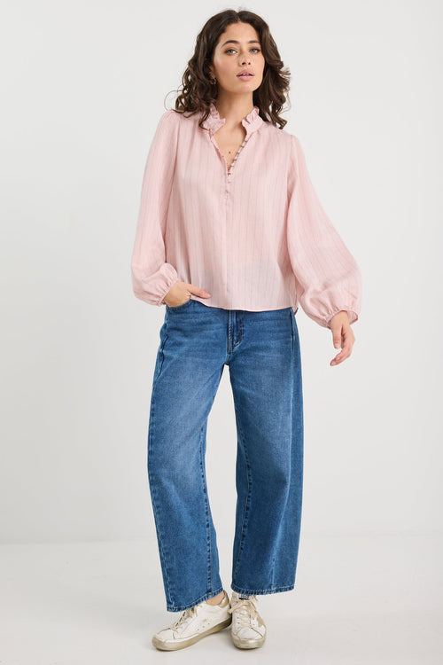 Woman wearing a light pink blouse and blue jeans on a white background