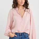 Woman wearing a light pink blouse and blue jeans against a white background