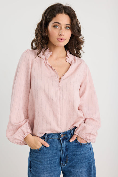 Woman wearing a light pink blouse and blue jeans against a plain background