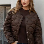 Woman wearing a brown quilted jacket against a light-colored wall.