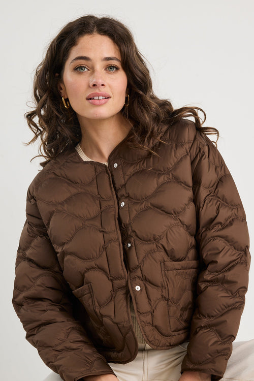 Woman wearing a brown quilted jacket sitting on a white surface