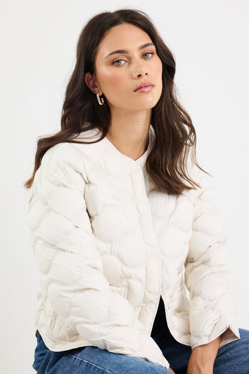Woman wearing a white quilted jacket and blue jeans against a white background