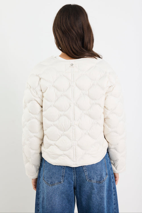 Person wearing a white quilted jacket and blue jeans on a plain background
col_pattern