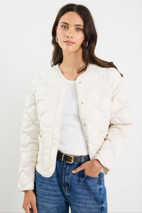 Woman wearing a white puffer jacket, white shirt, and blue jeans on a plain background