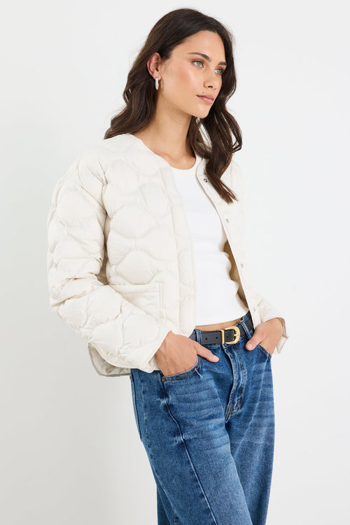 Woman wearing a white puffer jacket and blue jeans on a plain background