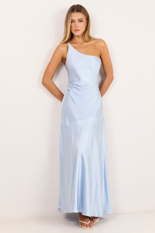 A woman modeling a light blue one-shoulder satin maxi dress against a plain off-white studio background.