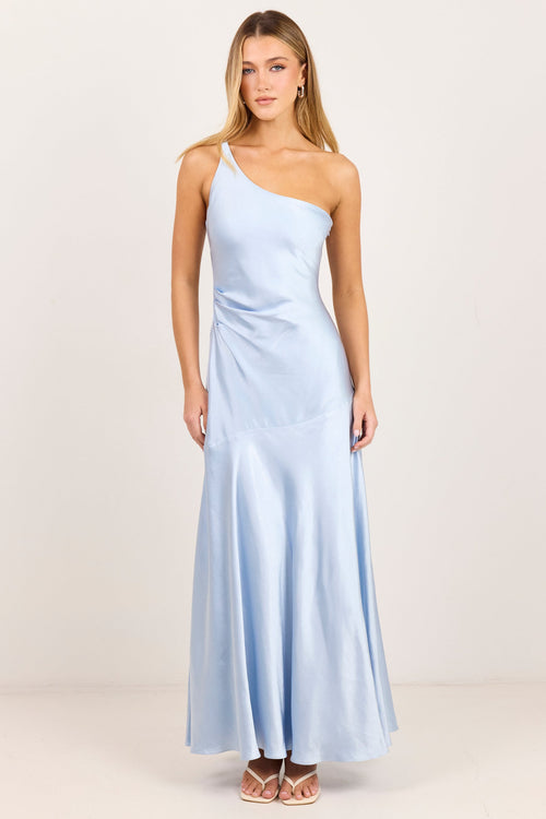 A woman modeling a light blue satin one-shoulder maxi dress against a plain off-white studio background.