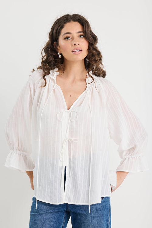 Woman wearing a white blouse and blue jeans against a plain background