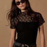 Woman wearing a black lace top and high-waisted black pants against a brown background