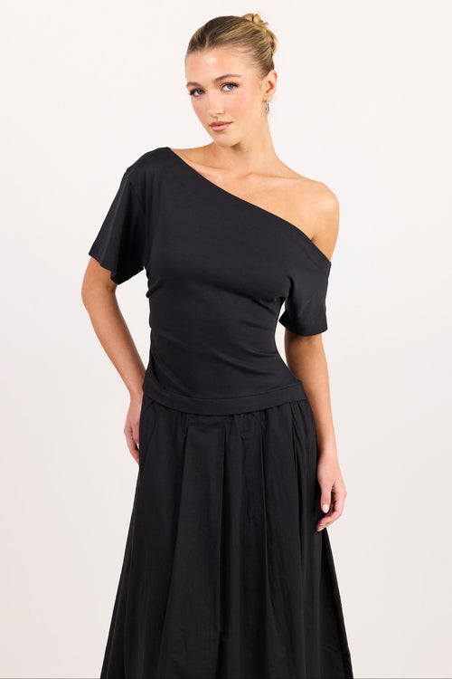 A woman modeling a black one-shoulder short-sleeve dress with a pleated skirt against a plain light background.