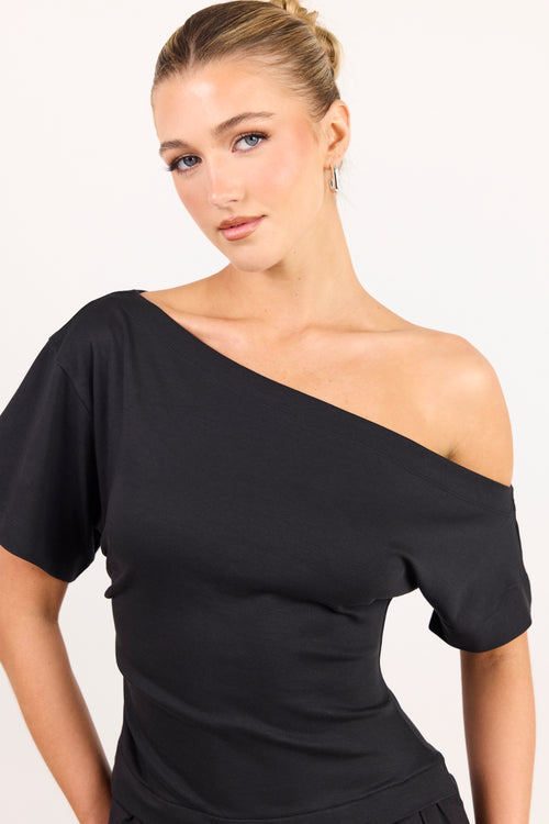A woman modeling a black off-the-shoulder short-sleeve top against a plain white studio background.