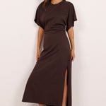 A woman modeling a dark brown short-sleeve midi dress with a high side slit, styled with black sunglasses and black heeled sandals against a plain white studio background.