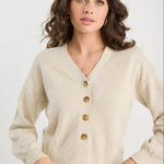 Woman wearing a beige cardigan with gold buttons on a white background