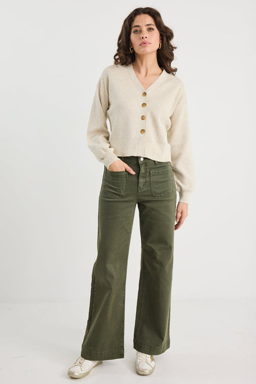 Woman wearing a beige cardigan and green pants on a white background