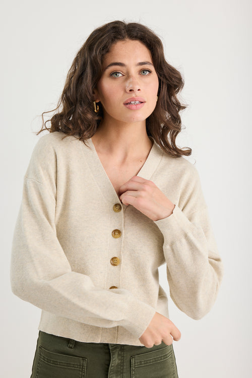 Woman wearing a beige cardigan with gold buttons on a white background