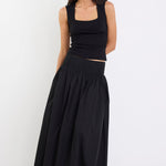 Woman wearing a black sleeveless top and long black skirt on a white background