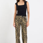 Woman wearing a black sleeveless top and leopard print pants on a white background