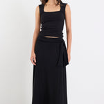 Woman wearing a black sleeveless top and long black skirt on a white background