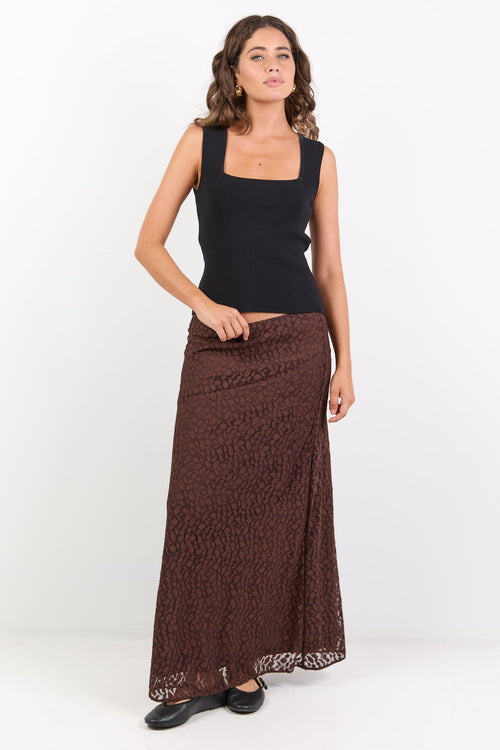 Woman wearing a black top and brown patterned skirt on a white background