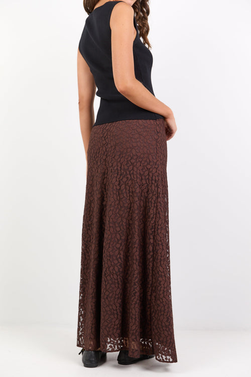 Person wearing a black sleeveless top and brown patterned skirt on a white background