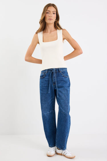 Woman wearing a white tank top and blue jeans on a white background