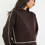 Woman wearing a brown sweater with white trim on a plain background