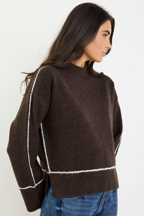 Woman wearing a brown sweater with white trim on a plain background