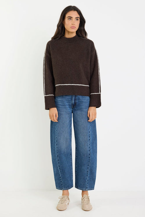 Woman wearing a brown sweater and blue jeans on a white background