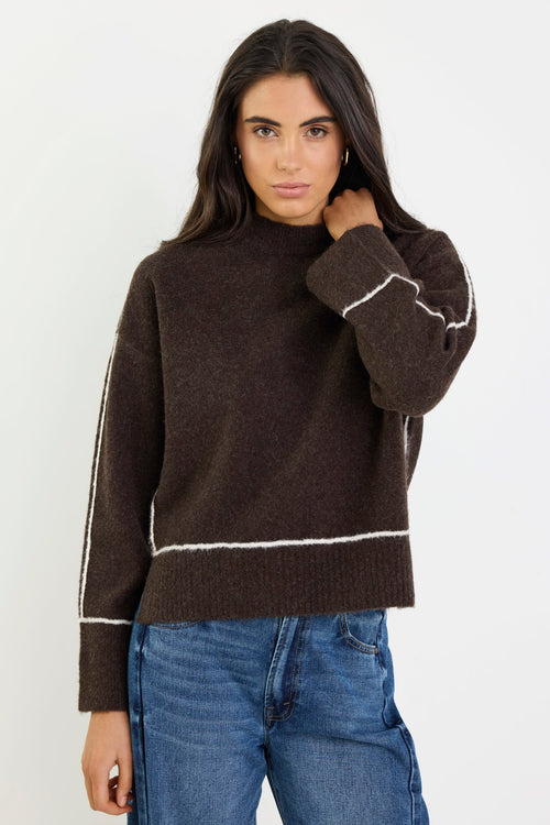 Woman wearing a brown sweater with white trim and blue jeans on a white background