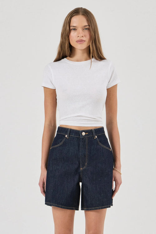 Woman wearing a white crop top and dark denim skirt on a white background