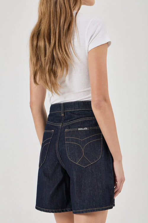 Person wearing a white t-shirt and dark denim shorts on a plain background