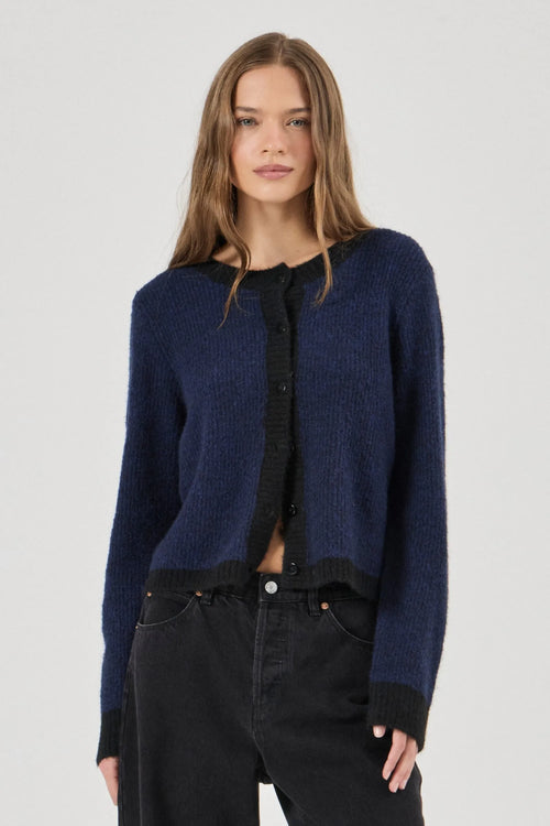 Woman wearing a blue cardigan over a black shirt and pants on a white background