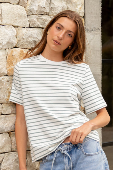 Woman wearing a striped shirt and jeans standing against a stone wall.