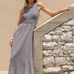 Woman in a gray dress standing against a beige wall with stone architecture.