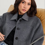 Woman sitting on a modern chair wearing a gray coat and light blue jeans.