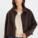 Woman wearing a brown jacket over a beige sweater and blue jeans on a white background