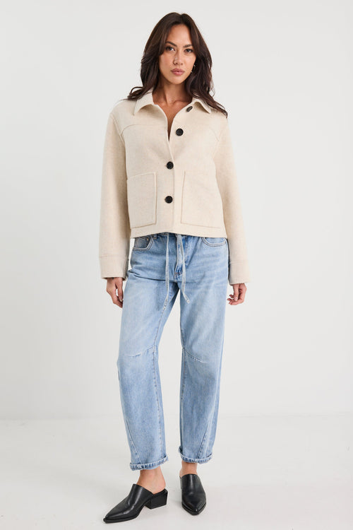 Woman wearing a beige jacket and light blue jeans on a white background