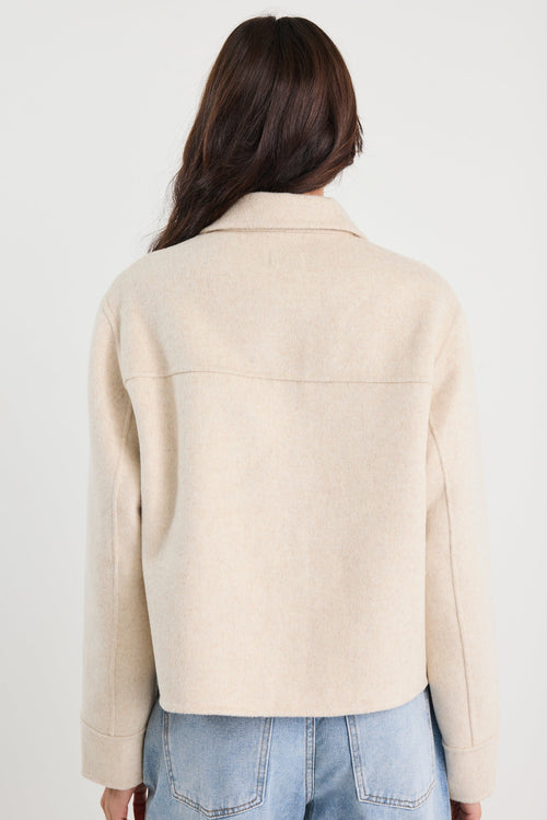 Person wearing a beige jacket and blue jeans on a white background