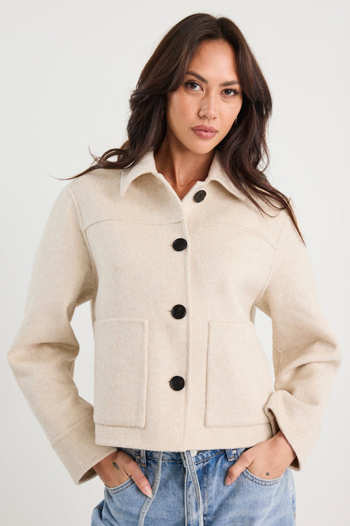 Woman wearing a beige jacket with black buttons on a white background
