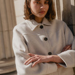 Woman wearing a light-colored coat standing against a neutral background
