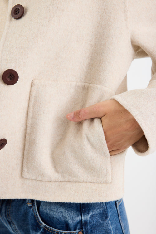 Close-up of a person wearing a beige jacket with brown buttons and blue jeans.