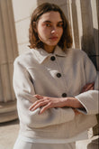 Woman wearing a light-colored coat standing against a neutral background