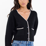 Woman wearing a black cardigan with white trim and blue jeans on a white background