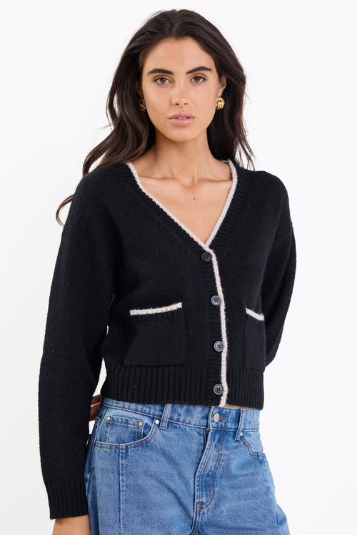Woman wearing a black cardigan with white trim and blue jeans on a white background