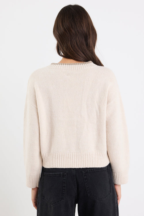 Person wearing a cream sweater and black pants on a white background