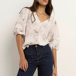 Woman wearing an ivory floral V-neck blouse with ruched puff sleeves, styled with dark indigo denim.