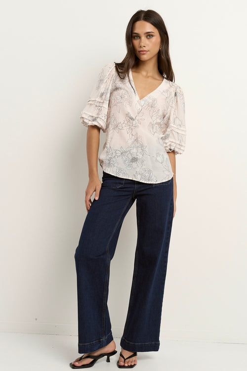 Woman wearing an ivory floral V-neck blouse with ruched puff sleeves, styled with dark indigo denim.