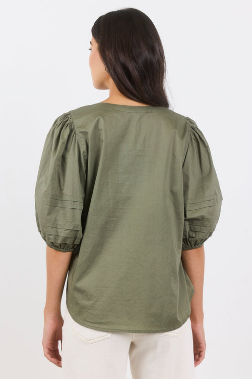 Woman wearing an olive green blouse with puffed sleeves on a white background