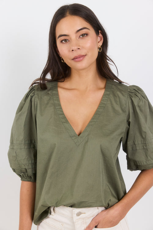 Woman wearing a green blouse with puffed sleeves against a white background